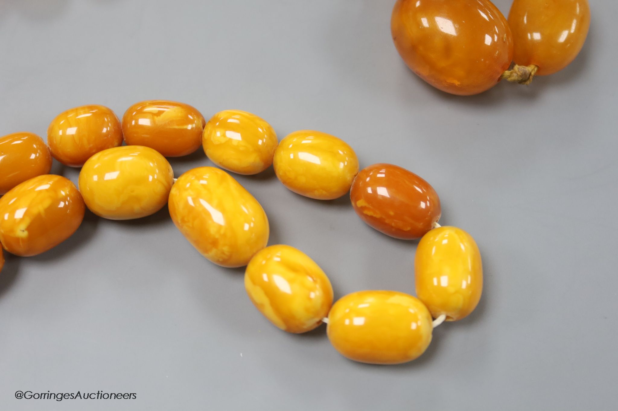 Two single strand graduated oval amber bead necklaces, 71cm, 61 grams & 89cm, 68 grams (beads missing from larger necklace)